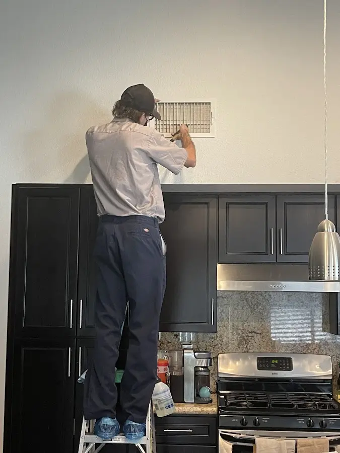 Technician inspecting an air vent during HVAC service in Logan